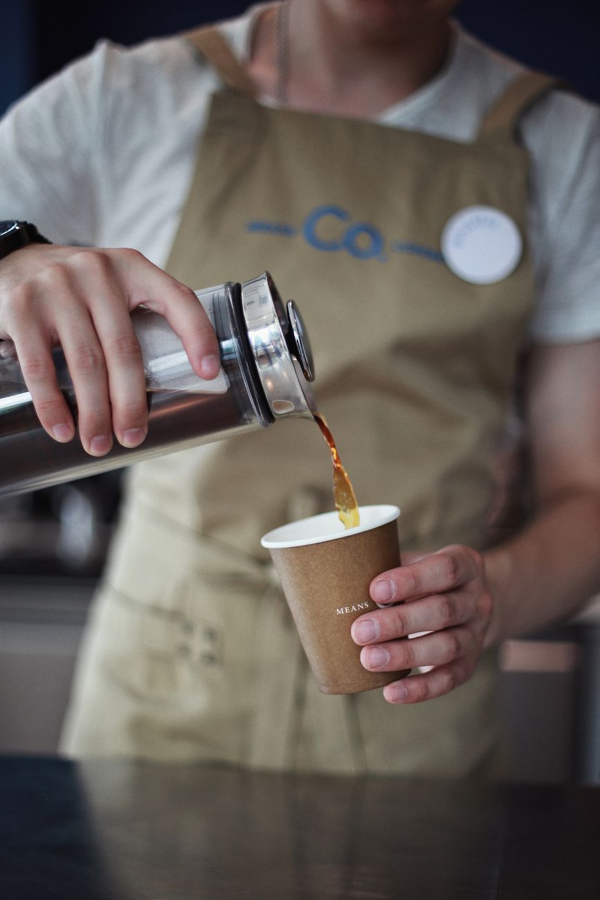 Barista in Schürze gießt ein frisch zubereitetes Getränk ein