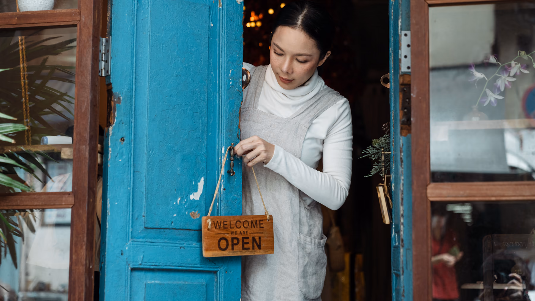 Eine Ladeninhaberin hängt das Schild „Open“ an die Tür.